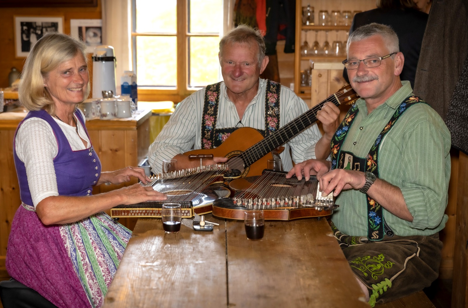 Wackersberger Zithermusi Hanni und Franz Apfel sowie Klaus Stumpf, sitzend am Tisch mit Zither und Gitarre