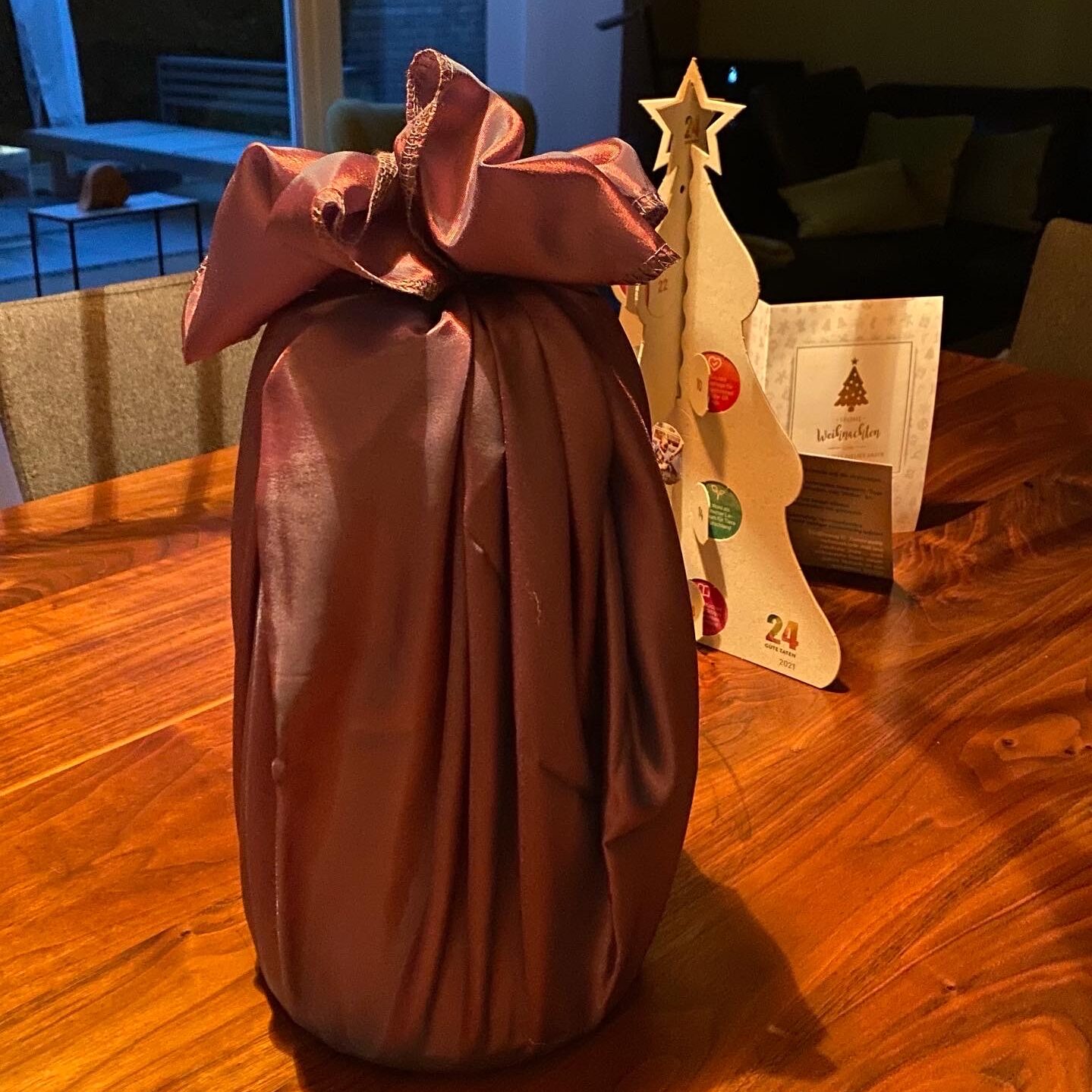 eingepacktes Geschenk mit Furoshiki-Tuch Ein Geschenk, welches mit einem roten Tuch eingepackt ist und auf deinem Holztisch steht.